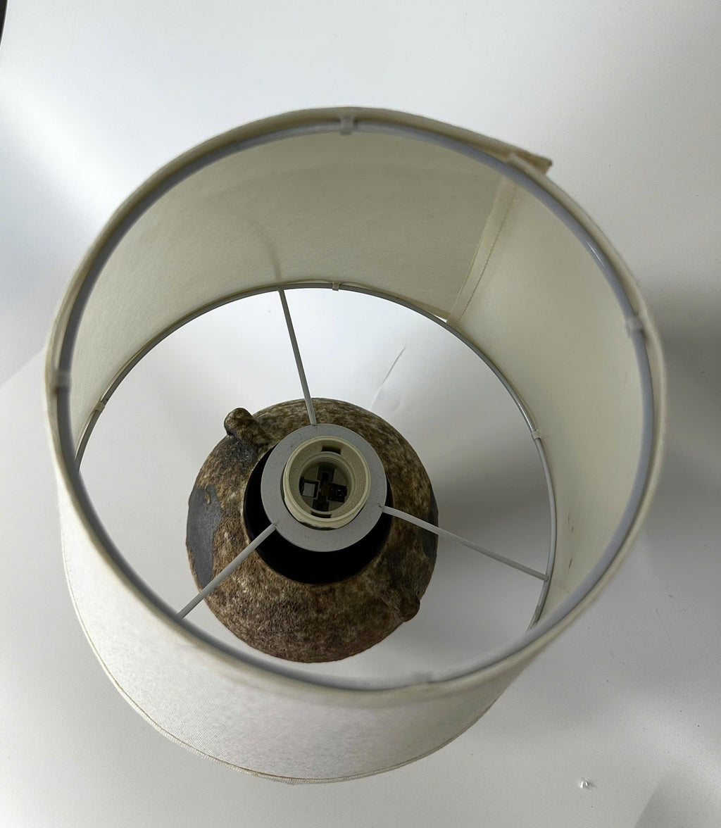 Handmade ceramic table lamp with ancient side handles, a wabi-sabi silhouette, and soft fabric shade casting a warm, timeless glow.