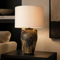 Handmade ceramic table lamp with ancient side handles, a wabi-sabi silhouette, and soft fabric shade casting a warm, timeless glow.